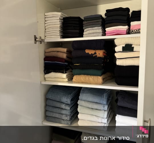 בגדים מקופלים ומסודרים בארון לבן עם מדפים